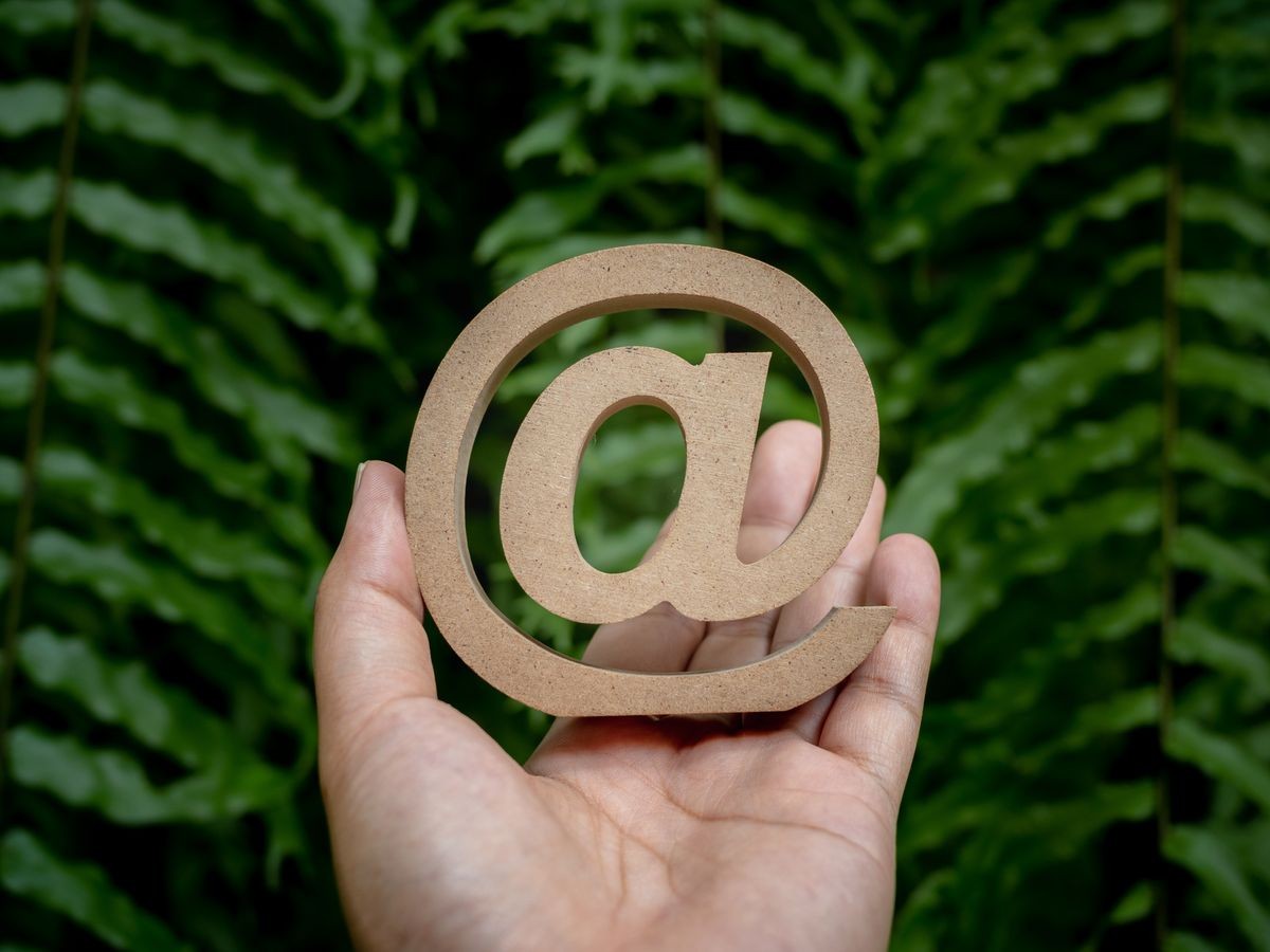 Wooden E-mail address symbol on left hand, arroba icon on green leaves background. E-mail marketing online internet, technology and environment concept.